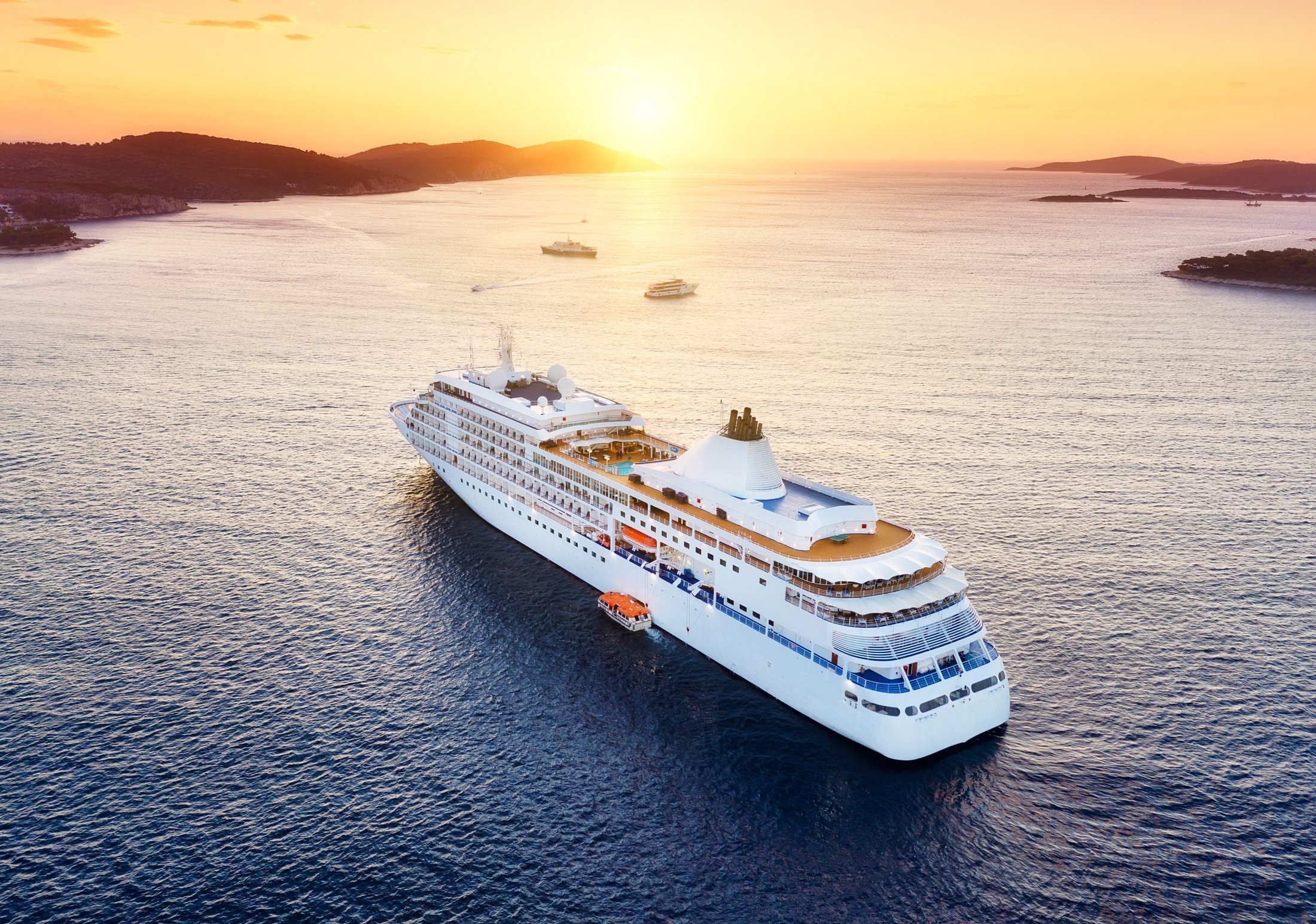 A luxury cruise ship sailing across calm seas toward a golden sunset