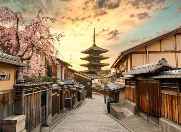 A quiet Kyoto street lined with traditional wooden houses, cherry blossoms, and a five-story pagoda