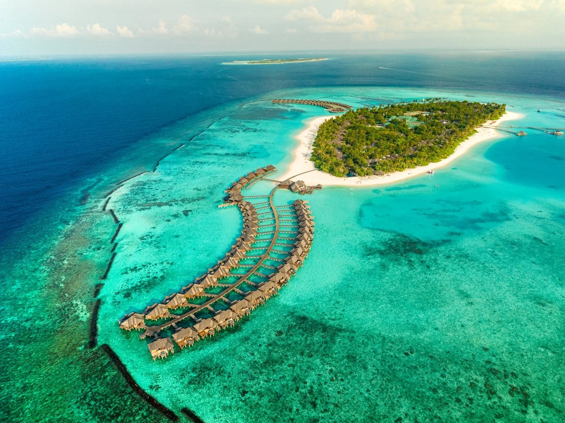 Aerial view of overwater villas curving into a turquoise Maldives lagoon